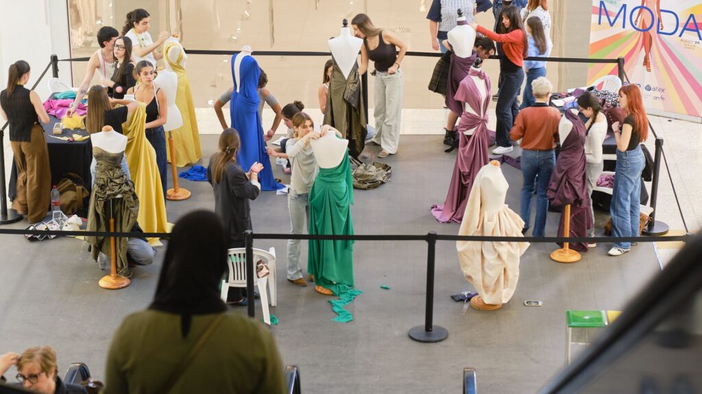 Vista elevada del taller en vivo de moulage en el Centro Comercial Alzamora, con multitud de estudiantes de diseño creando prendas sobre maniquíes durante la IV Semana de la Moda de Alcoy.